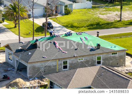 Workers installing asphalt shingles on suburban home rooftop. Roof construction for American housing project. Workers installing asphalt shingles on suburban home rooftop. Roof construction for American housing project. 143589833