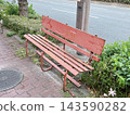 A nostalgic red steel retro bench stands beside the sidewalk. 143590282