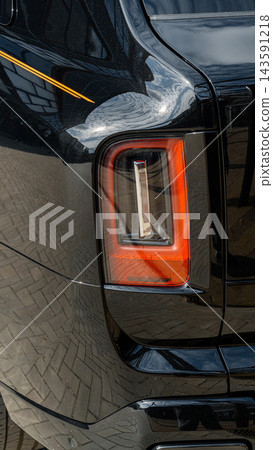 Luxury car tail light shines in urban setting with reflections and textured pavement Luxury car tail light shines in urban setting with reflections and textured pavement 143591218