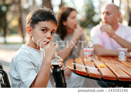 Child drinks soda at a table with family in a park during the afternoon 143591540