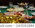 Christmas Eve dinner table decorating for a festive family gathering, featuring homemade gourmet appetizers, ham, cheese, and holiday tinsel creating a cheerful party atmosphere 143591884