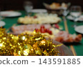 Christmas Eve dinner table showcasing a gourmet spread with ham and cheese platters, gold tinsel decorations, and blurred festive holiday food for a family celebration party 143591885