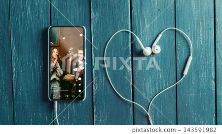 Social media chats and calls with friends using a phone and headphones on a wooden table Social media chats and calls with friends using a phone and headphones on a wooden table 143591982
