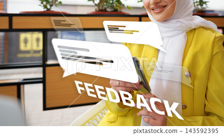 Woman in a yellow jacket sitting in cafe while using her phone and engaging with feedback Woman in a yellow jacket sitting in cafe while using her phone and engaging with feedback 143592395