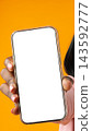 Person holds a smartphone with a blank screen in front of an orange background 143592777