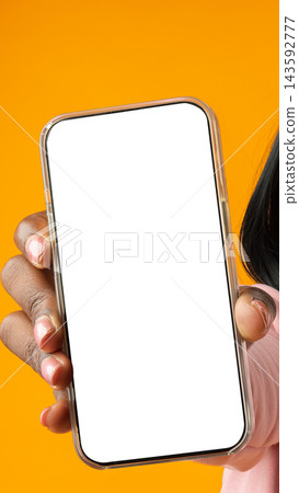 Person holds a smartphone with a blank screen in front of an orange background Person holds a smartphone with a blank screen in front of an orange background 143592777
