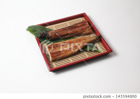 Grilled eel cut in half, served on a bamboo leaf and a bamboo mat base. Grilled eel cut in half, served on a bamboo leaf and a bamboo mat base. 143594800