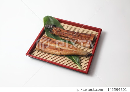 Grilled eel cut in half, served on a bamboo leaf and a bamboo mat base. Grilled eel cut in half, served on a bamboo leaf and a bamboo mat base. 143594801