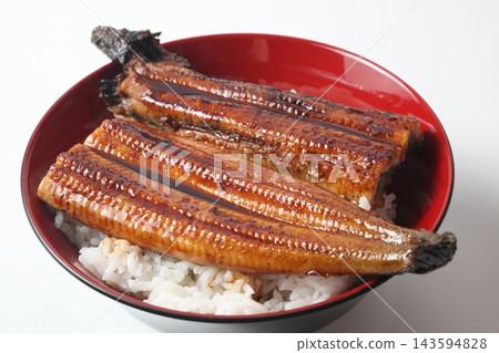 A close-up of a rice bowl topped with glossy grilled eel. A close-up of a rice bowl topped with glossy grilled eel. 143594828