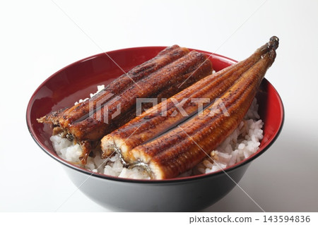 A close-up of a rice bowl topped with glossy grilled eel. A close-up of a rice bowl topped with glossy grilled eel. 143594836