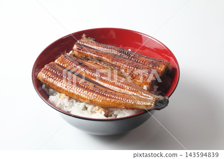 A close-up of a rice bowl topped with glossy grilled eel. A close-up of a rice bowl topped with glossy grilled eel. 143594839