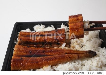 A piece of eel bento (unaju) lifted with chopsticks. A piece of eel bento (unaju) lifted with chopsticks. 143594883
