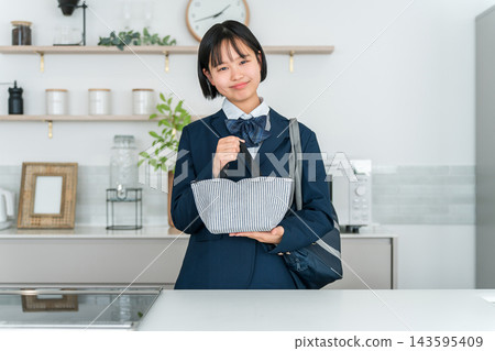 一名身穿制服的高中女生在家裡的廚房裡,把午餐放進保溫袋裡,準備帶去學校。 一名身穿制服的高中女生在家裡的廚房裡,把午餐放進保溫袋裡,準備帶去學校。 143595409