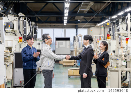 在製造廠,公司貸款協議最終敲定,公司管理層與銀行代表握手,員工們鼓掌慶祝。 在製造廠,公司貸款協議最終敲定,公司管理層與銀行代表握手,員工們鼓掌慶祝。 143595648