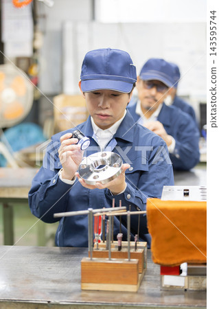 一位年輕的男工程師在製造廠使用帶燈的放大鏡來目視檢查精密金屬零件。 一位年輕的男工程師在製造廠使用帶燈的放大鏡來目視檢查精密金屬零件。 143595744