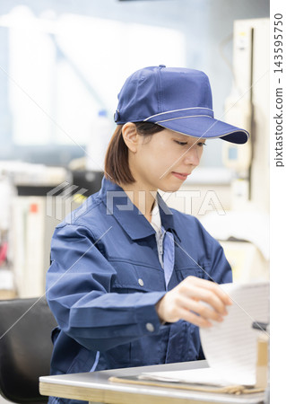 一位年輕的女技術員坐在製造廠檢驗室的顯微鏡旁,查看品質控制檢驗記錄和文件。 一位年輕的女技術員坐在製造廠檢驗室的顯微鏡旁,查看品質控制檢驗記錄和文件。 143595750