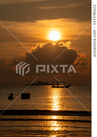 Captivating golden sunset over a tropical sea, featuring the sun reflecting on the calm water. Silhouettes of a boat, a person wading, and a distant island create a serene scene. Captivating golden sunset over a tropical sea, featuring the sun reflecting on the calm water. Silhouettes of a boat, a person wading, and a distant island create a serene scene. 143596022