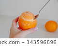 Hand holds a frozen orange filled with homemade sorbet while a spoon scoops the creamy dessert from the fruit peel. Serving idea for dairy free dessert recipes and summer menus. 143596696