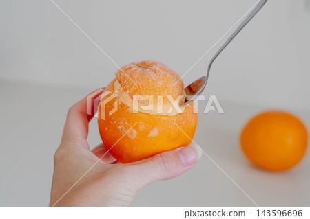 Hand holds a frozen orange filled with homemade sorbet while a spoon scoops the creamy dessert from the fruit peel. Serving idea for dairy free dessert recipes and summer menus. Hand holds a frozen orange filled with homemade sorbet while a spoon scoops the creamy dessert from the fruit peel. Serving idea for dairy free dessert recipes and summer menus. 143596696