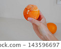 Hand holds a frozen orange filled with homemade sorbet while a spoon scoops the creamy dessert from the fruit peel. Serving idea for dairy free dessert recipes and summer menus. 143596697