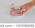 A female hand touches the spiked surface of a ceramic grater plate beside a garlic bulb and a separate clove on a white table. Handmade kitchen tool for grating garlic, ginger and vegetables. 143596698