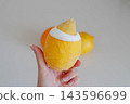 A hand holds a frozen lemon filled with homemade lemon gelato next to a fresh whole lemon against a neutral backdrop. Dessert idea for an artisan ice cream shop menu and summer recipe blog. 143596699