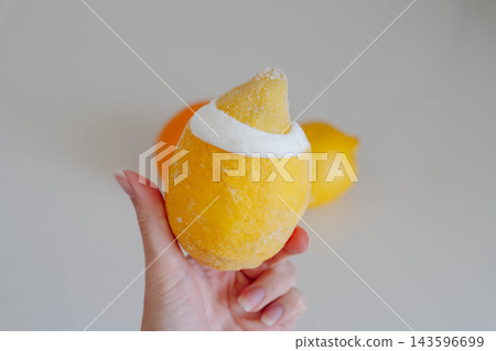 A hand holds a frozen lemon filled with homemade lemon gelato next to a fresh whole lemon against a neutral backdrop. Dessert idea for an artisan ice cream shop menu and summer recipe blog. A hand holds a frozen lemon filled with homemade lemon gelato next to a fresh whole lemon against a neutral backdrop. Dessert idea for an artisan ice cream shop menu and summer recipe blog. 143596699