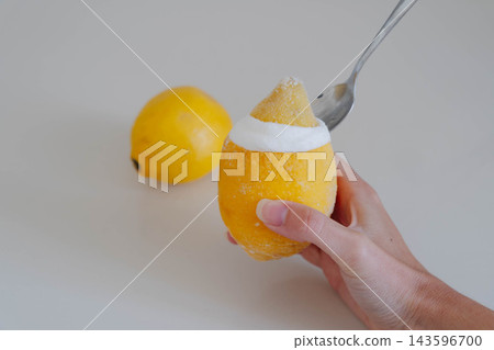Hand holds a frozen lemon stuffed with sorbet beside a spoon and a whole fresh lemon on a light table. Homemade citrus dessert idea for recipe blogs, summer menus and cafe promotions. Hand holds a frozen lemon stuffed with sorbet beside a spoon and a whole fresh lemon on a light table. Homemade citrus dessert idea for recipe blogs, summer menus and cafe promotions. 143596700