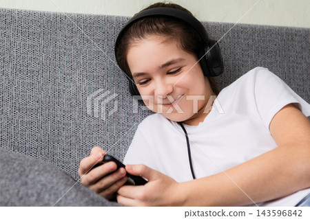 Young girl relaxed on couch listening to music on smartphone with headphone and smiling 143596842