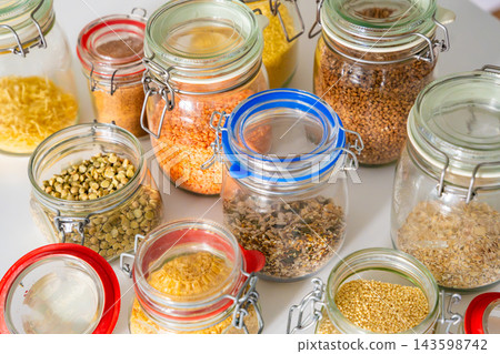 Assorted grains, legumes and seeds stored in glass jars with clasp lids on a kitchen counter. Organized pantry storage supports meal planning and a low waste household lifestyle 143598742