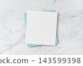 Top view of blank white and blue square greeting card mockup on marble background with copy space 143599398