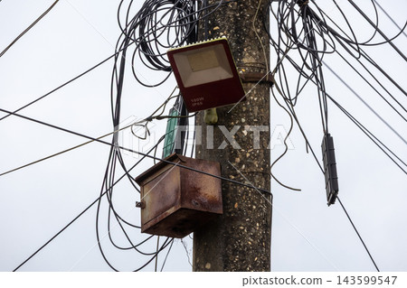 Close-up shot of an LED floodlight mounted on a concrete pole surrounded by messy tangled electrical wires. Close-up shot of an LED floodlight mounted on a concrete pole surrounded by messy tangled electrical wires. 143599547