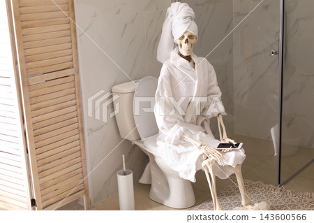 Skeleton in bathrobe with mobile phone sitting on toilet bowl Skeleton in bathrobe with mobile phone sitting on toilet bowl 143600566