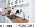 Side angle of a black cooking surface on wooden countertop in a minimalist bright white kitchen, home design, cozy lifestyle. 143601264