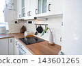 Modern kitchen counter with black electrical stovetop wooden surface and hanging kitchen utensils, home design, cozy lifestyle. 143601265