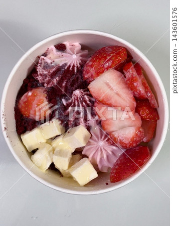 Swirled yogurt ice cream dessert served in a cup, smooth creamy texture with glossy surface, topped with fresh fruit pieces, highlighting its refreshing and inviting appearance in detail 143601576