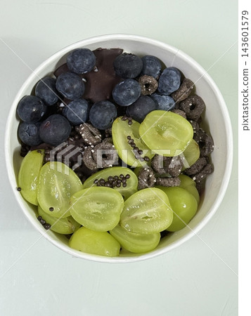 Swirled yogurt ice cream dessert served in a cup, smooth creamy texture with glossy surface, topped with fresh fruit pieces, highlighting its refreshing and inviting appearance in detail 143601579