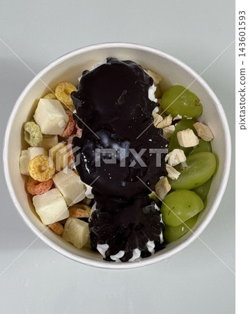 Swirled yogurt ice cream dessert served in a cup, smooth creamy texture with glossy surface, topped with fresh fruit pieces, highlighting its refreshing and inviting appearance in detail 143601593