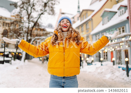 Smiling woman in a bright jacket is having fun with the snow on a snowy city street. Smiling woman in a bright jacket is having fun with the snow on a snowy city street. 143602011