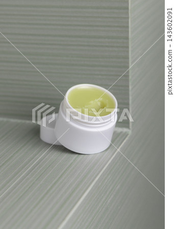 Open lip balm jar with a lid in green bathroom. Handmade herbal cosmetic product for home use 143602091