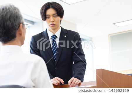 A young male prosecutor questions a man in a courtroom. A young male prosecutor questions a man in a courtroom. 143602139