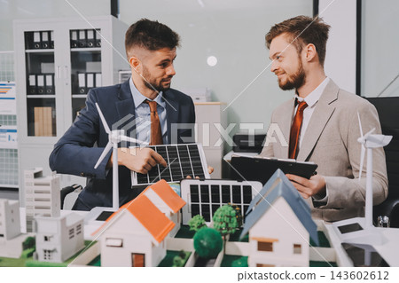 Team presenting a solar and wind energy project with model house, earth globe and green ideas in an office meeting Team presenting a solar and wind energy project with model house, earth globe and green ideas in an office meeting 143602612