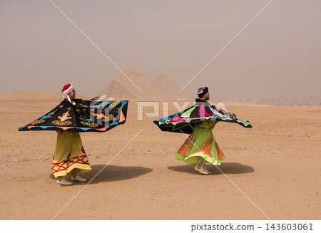 Two Egyptian sufi whirling dervish performers spinning vibrant colorful robes at the Great Pyramids of Giza in Egypt ideal for travel tourism and MENA Two Egyptian sufi whirling dervish performers spinning vibrant colorful robes at the Great Pyramids of Giza in Egypt ideal for travel tourism and MENA 143603061