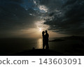 Couple embracing passionately by seaside at sunset with dramatic clouds and warm light 143603091
