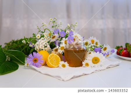 Golden honey is traditionally enjoyed with warm tea and fresh lemon during the cold season. A natural food ingredient presented with bright flowers and citrus on a clean white background. Golden honey is traditionally enjoyed with warm tea and fresh lemon during the cold season. A natural food ingredient presented with bright flowers and citrus on a clean white background. 143603352