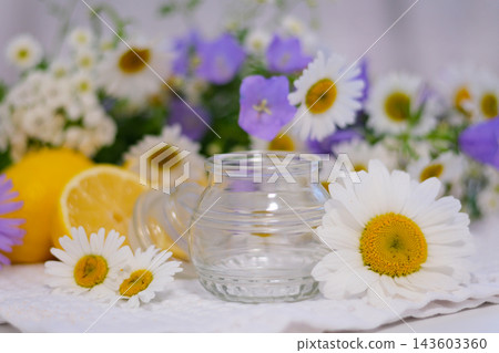 Empty glass jar surrounded by white daisies and blue wildflowers creating bright natural summer composition close up Empty glass jar surrounded by white daisies and blue wildflowers creating bright natural summer composition close up 143603360