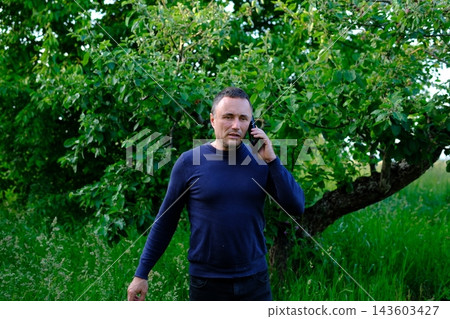 Middle aged man having serious phone conversation outdoors near green trees discussing important personal or business matters Middle aged man having serious phone conversation outdoors near green trees discussing important personal or business matters 143603427