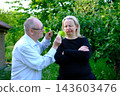 Senior father offering fresh lettuce from garden to adult daughter while encouraging healthy eating in countryside yard 143603476