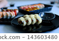 Assorted sushi platter with various types of nigiri, maki rolls, and sashimi on black plate, showcasing Japanese cuisine. Authentic Japanese Food and Culinary Arts. 143603480