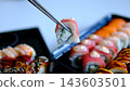 Sushi delivery set with tuna rolls in black containers, chopsticks dipping into soy sauce during takeaway meal presentation 143603501